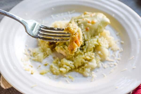 Bite of the baked pesto chicken recipe on a fork above a plate of pesto chicken.