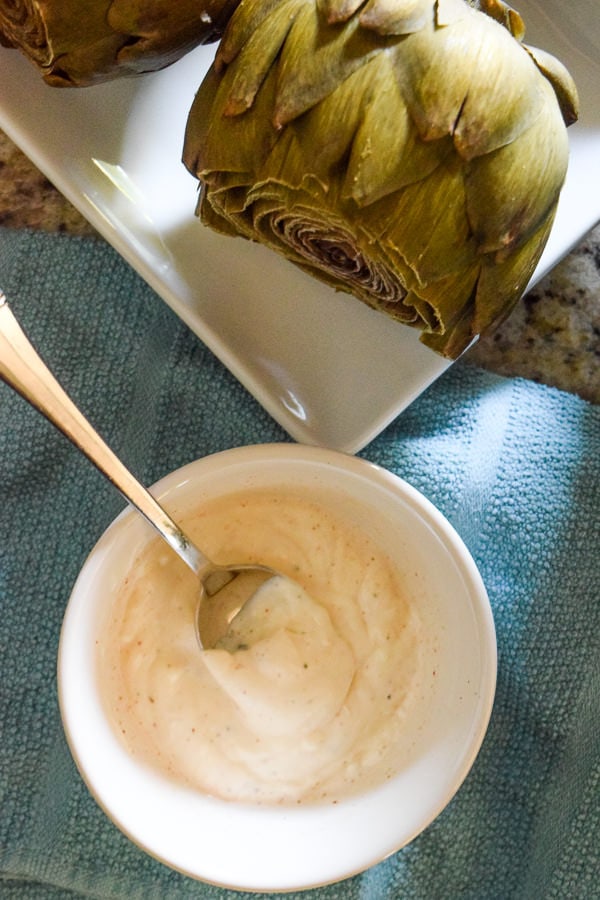 Close up of creamy chili dipping sauce next to a plate of instant pot artichokes.