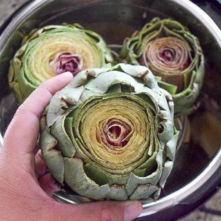 Three raw artichokes in an instant pot. Once is in the process of being placed inside.