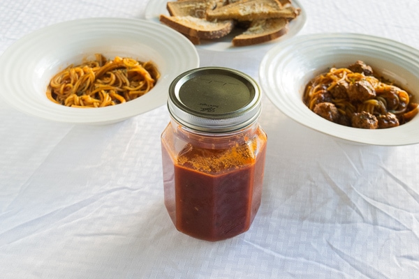 A mason jar filled with pressure cooker spaghetti sauce next to a bowl of spaghetti and meatballs and a bowl of plain spaghetti.