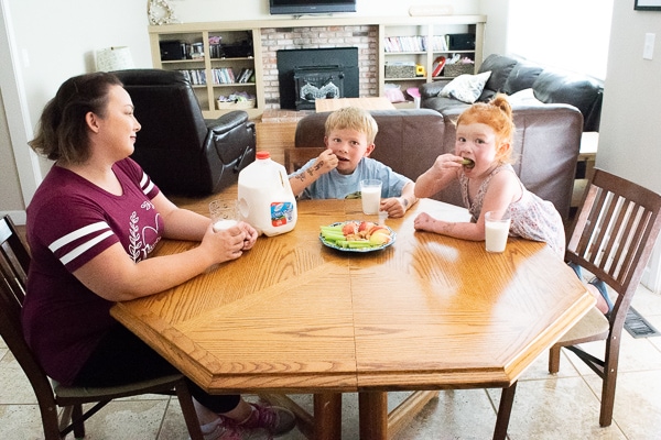 Two children sitting with their mother at a table eating snacks and dairy pure milk.