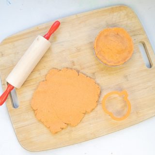 pumpkin pie play dough on a cutting board with a rolling pin and pumpkin cookie cutter.