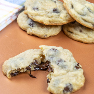 A salted chocolate chip cookie broken in half with the chocolate dripping out in front of a stack of cookies.