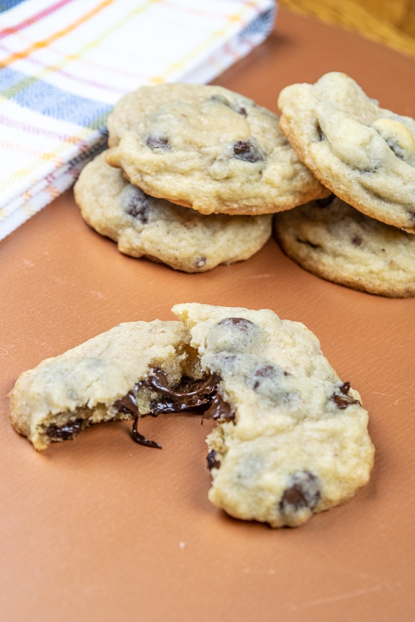 A salted chocolate chip cookie broken in half with the chocolate dripping out in front of a stack of cookies.