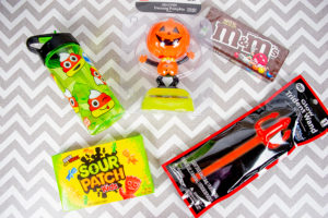 The contents of a BOO basket for a tween boy: two full sized candy bars glow stick, water bottle, and dancing pumpkin figurine.