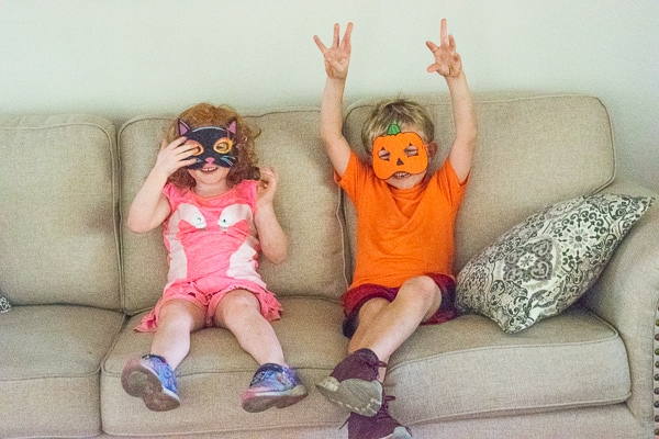 A boy and girl sitting on a couch and wearing Halloween masks.