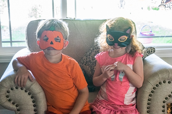 A boy and girl sitting together on a chair wearing masks.