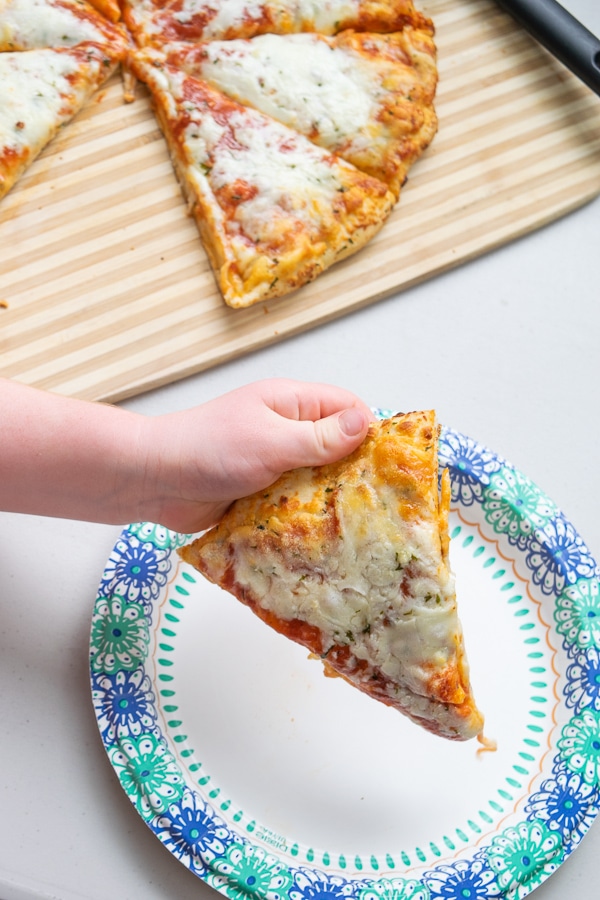 A child's hand holding a slice of cheese pizza.