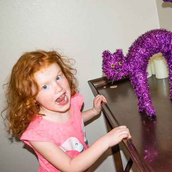 A red headed girl standing next to a purple cat decoration.