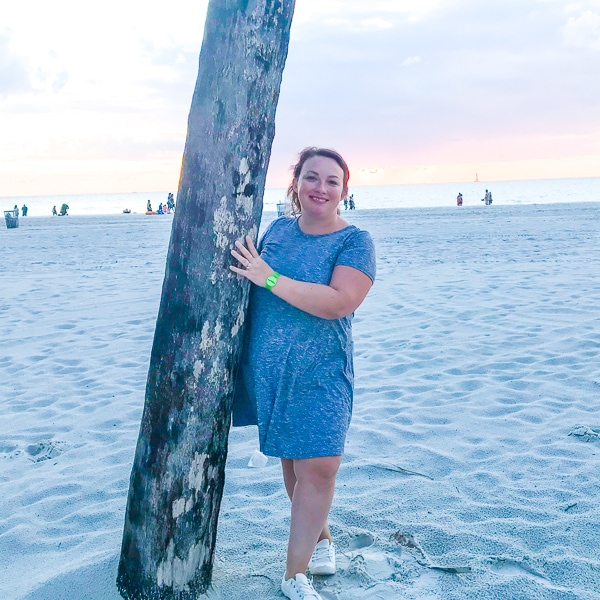 Women standing on the beach at sunset, leaning against a palm tree. 