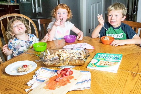 Three kids sitting around a table and taste-testing the apple-cinnamon french toast bake they made together.