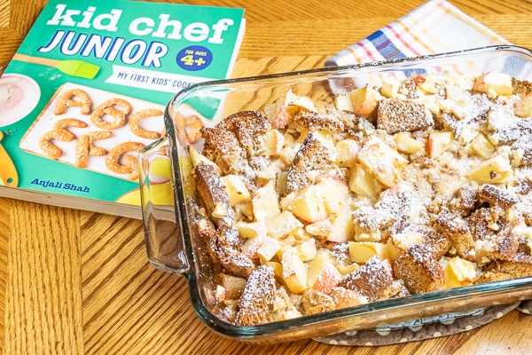 Apple cinnamon french toast bake on a wood table next to the kid chef junior cookbook.