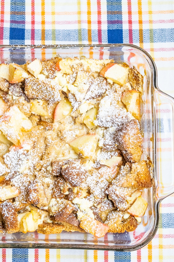 Apple-cinnamon french toast bake prepared in a glass baking dish and placed on a plaid tablecloth.