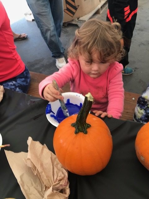 A toddler girl painting a pumpkin with blue paint during the Halloween festivities at Petaluma KOA.