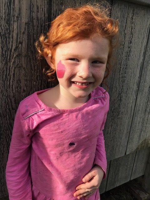 A red head 4 year old girl with a cupcake painted on her face.