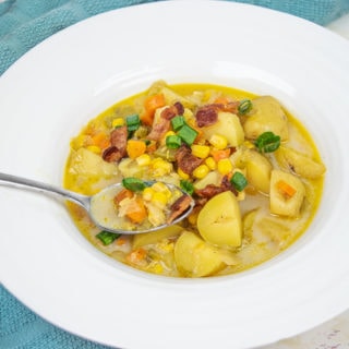 A white wide-rimmed bowl filled with instant pot potato corn chowder on a marble counter next to a blue dish towel.