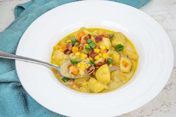 A white wide-rimmed bowl filled with instant pot potato corn chowder on a marble counter next to a blue dish towel.