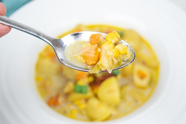 A spoonful of instant pot potato corn chowder right above the bowl of chowder.