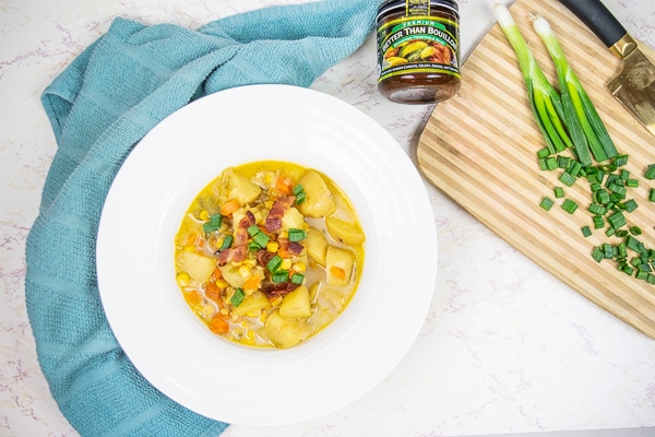 A big bowl of instant pot potato corn chowder net to a cutting board filled with sliced green onions.