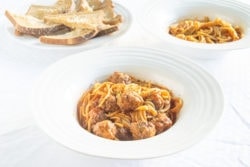 Two bowls of instant pot spaghetti and meatballs next to a plate of garlic toast.