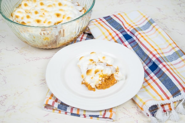 A bowl of instant pot sweet potato casserole behind a dish with a serving of the marshmallow topped side dish.