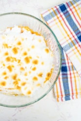 Sweet potato casserole served in a glass dish over a red and blue plaid dish towel.