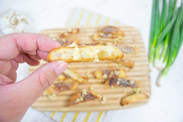 A hand holding a parmesan and garlic crisp over the tray full of parmesan and garlic crisps.