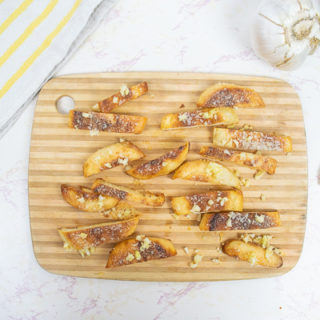 parmesan and garlic crisps on a wooden cutting board next to fresh garlic and scallions.