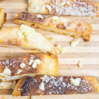 A close up shot of garlic and parmesan crisps on a cutting board.