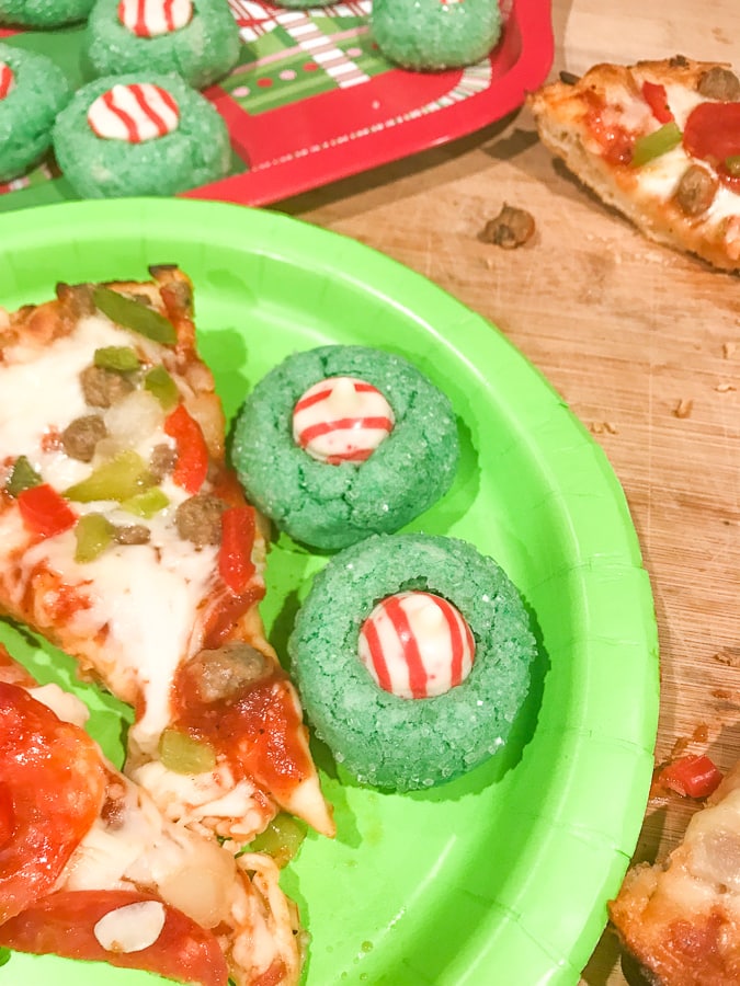 Grinch movie night dinner of supreme pizza and green grinch christmas cookies on a green paper plate.
