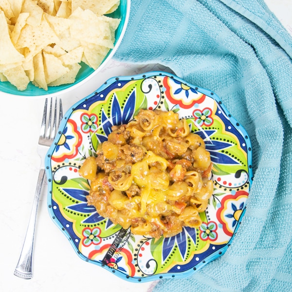 A bowl of tortilla chips next to a plate of instant pot taco pasta.
