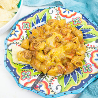 A colorful plate topped with a big portion of instant pot cheesy taco pasta next to a bowl full of tortilla chips.