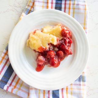 A white plate filled with instant pot cherry cobbler over a red and blue plaid dish towel.