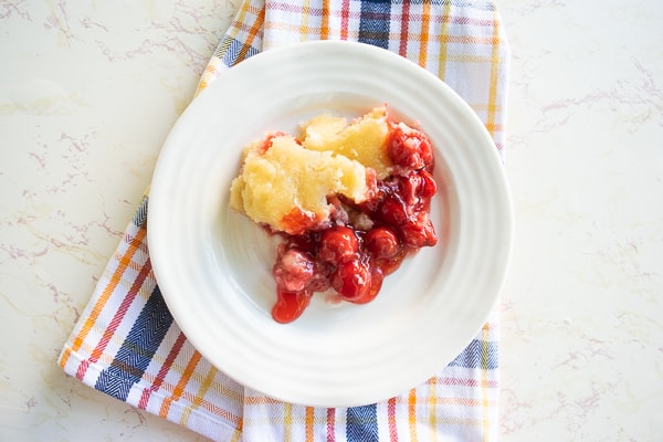 A white plate filled with instant pot cherry cobbler over a red and blue plaid dish towel.