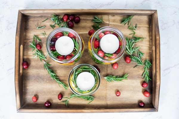 Mason jar christmas centerpieces arranged on a wooden serving tray.