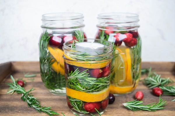 A side view of three mason jar Christmas centerpieces filled with cranberries and oranges.
