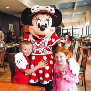 A boy and girl standing with Minnie Mouse at a Disneyland character breakfast.