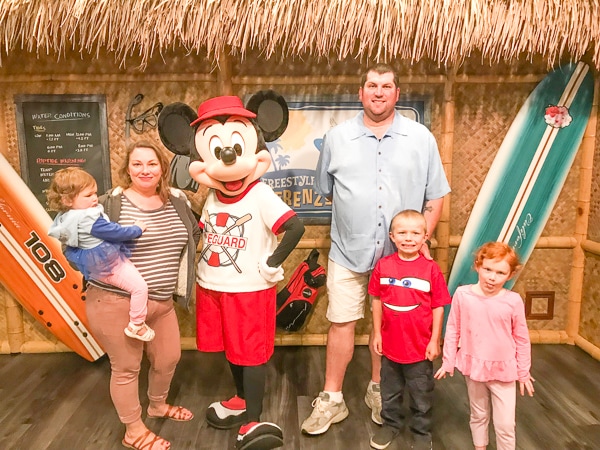 A woman and man with their three children, taking photo with Mickey Mouse at a character breakfast.