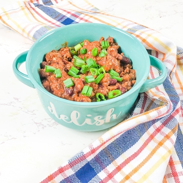 A bowl of instant pot beef chili next to a plaid dish towel.