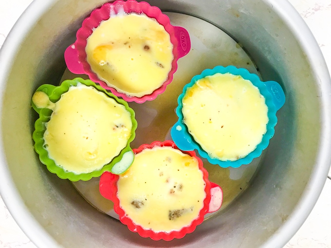4 cheesy sausage egg bites in colorful silicone muffin cups inside of an instant pot.