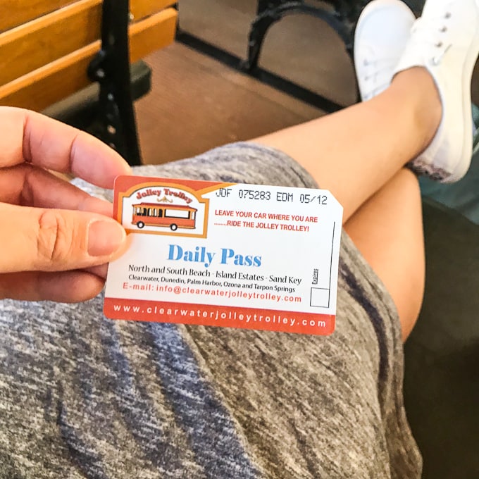 A woman holding a jolly trolly pass in front of her crossed legs stretched out over a bench.