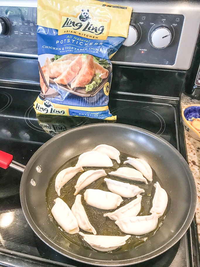 A pan of cooking potstickers next to a bag of Ling Ling chicken pot stickers. 