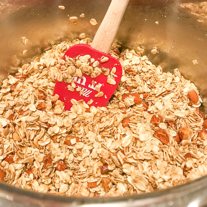 Granola in the instant pot getting stirred with a red rubber spatula.