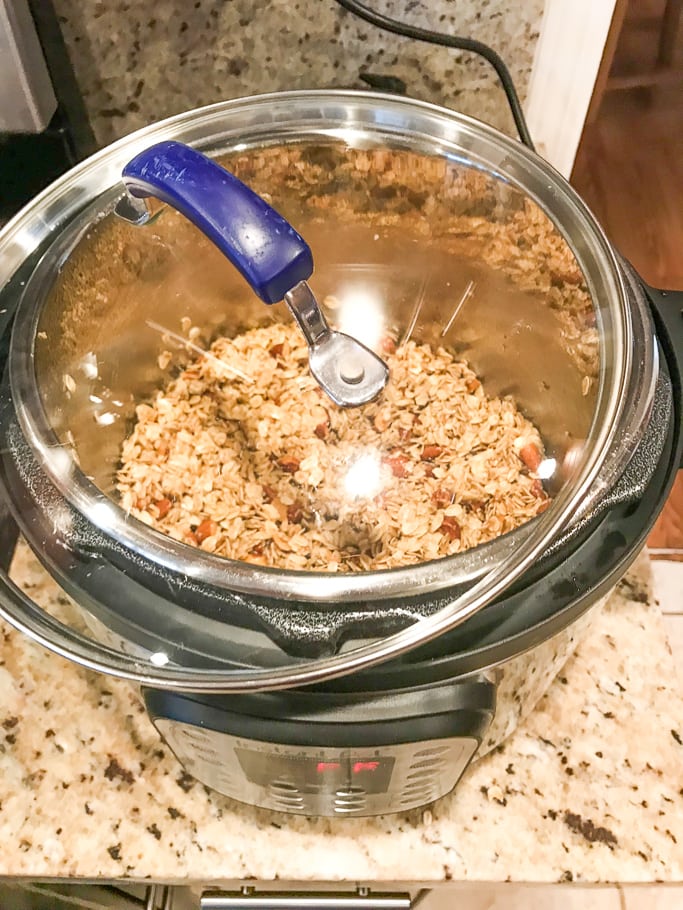An Instant Pot with granola inside and a glass lid partially covering the top.