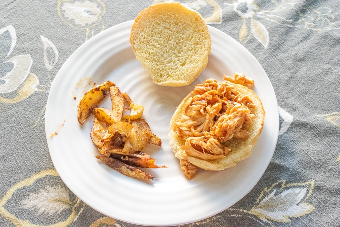 A plate of French fries and instant pot pulled chicken on a hamburger bun.