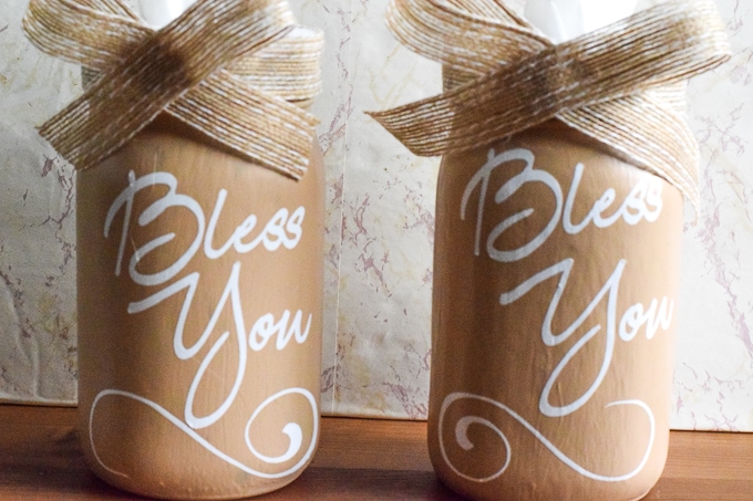 Two mason jars made into mason jar tissue holders and decorated with a ribbon bow.