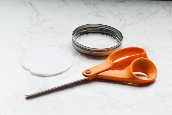 A pair of craft scissors next to the ring of a mason jar and a circle of white felt.