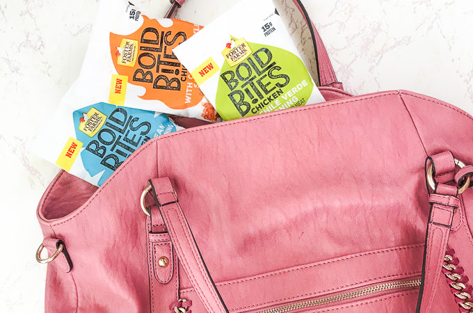 A large pink purse with three bags of Foster Farms Bold Bites poking out the top of the bag.