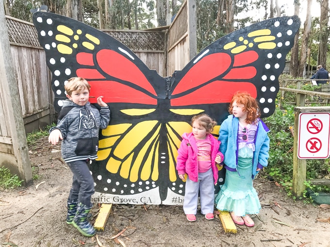 One boy and two girls standing in front of a 3-foot tall wooden butterfly at the Monarch Butterfly Sanctuary.