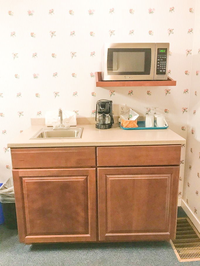 A kitchenette with a coffee maker, microwave, and coffee mugs.